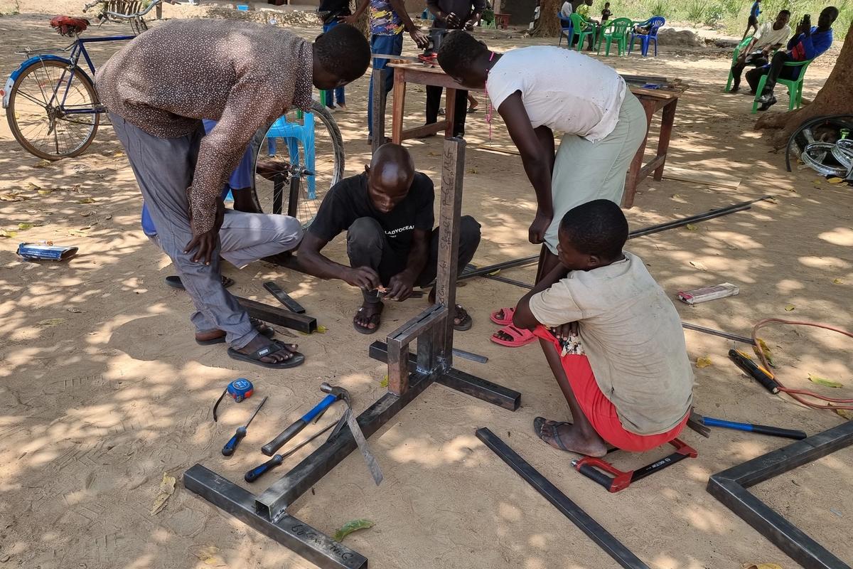 Designers gather around metal and wood pieces and tools while outside on a sunny day.